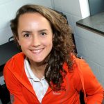 Lächelnde Ernährungsberaterin in orangefarbener Trainingsjacke für eine Ernährungsfirma.