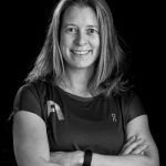 Frau mit verschränkten Armen und einem Lächeln, die ein Fitness-T-Shirt trägt.