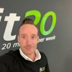 fit20 Coach lächelt im Studio, vor dem fit20 Logo. Er bewirbt 20 Minuten effektives Fitness-Training pro Woche.