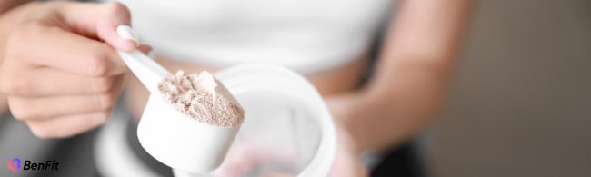 Nahaufnahme einer Frau, die BenFit Proteinpulver als Nahrungsergänzungsmittel mit einem Messlöffel aus einer Dose für ihre Fitness-Ernährung entnimmt.